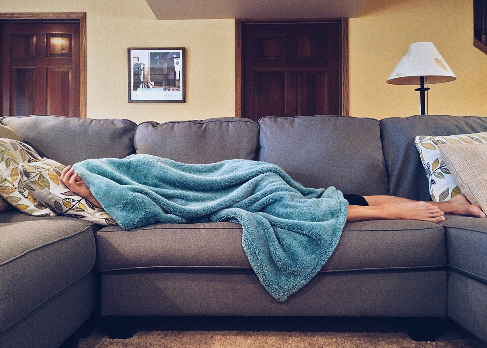 man lying on couch with blanket over head sick