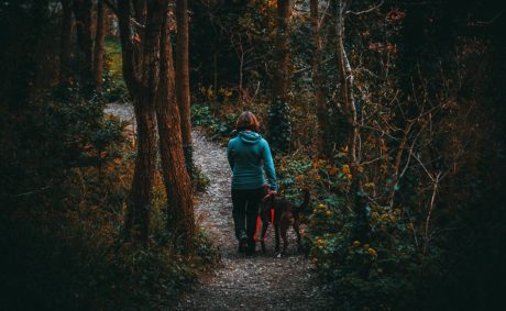 woman walking down wooded path with dog